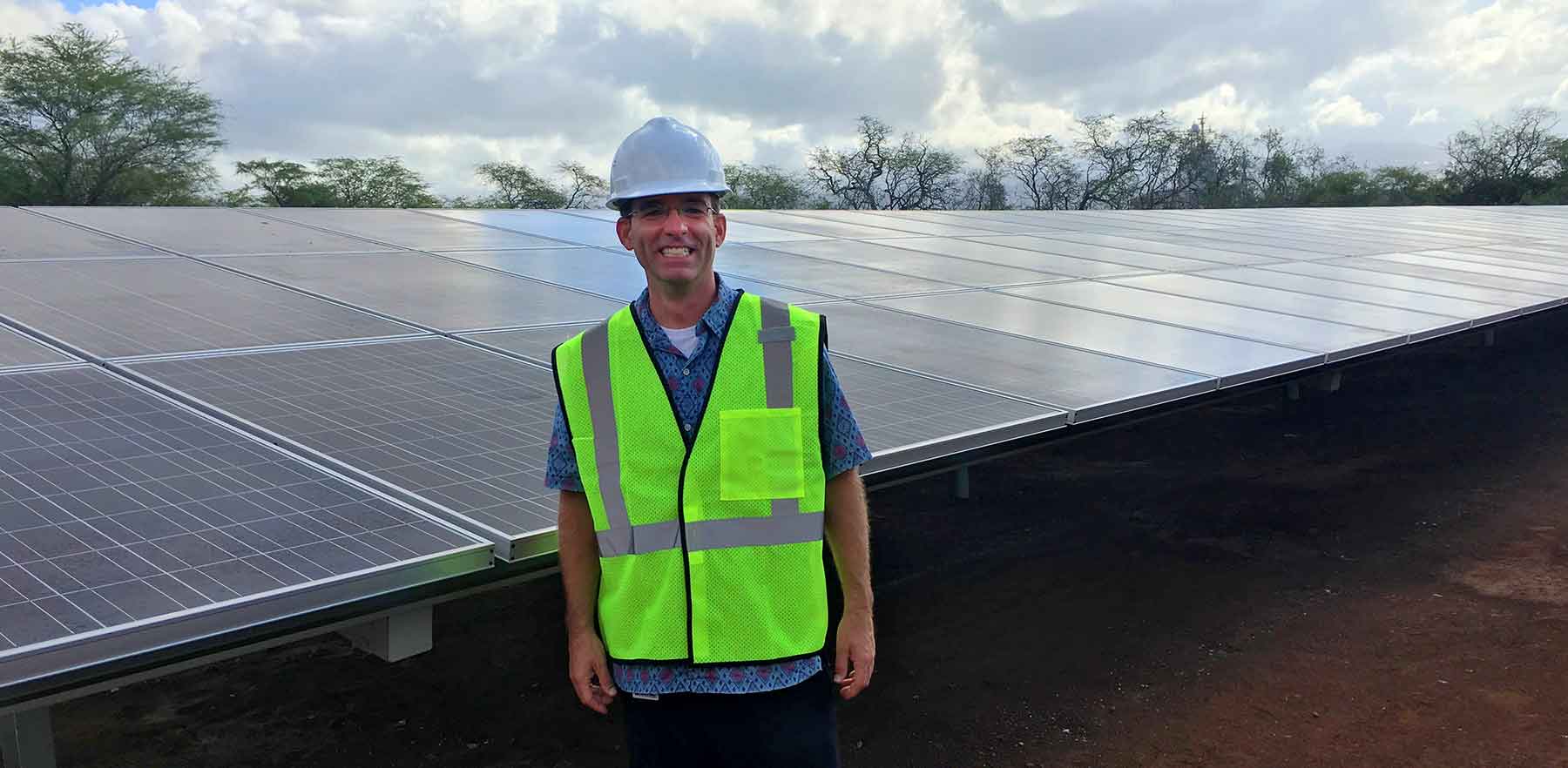  A man in a hard hat stands in front of an array of solar panels.