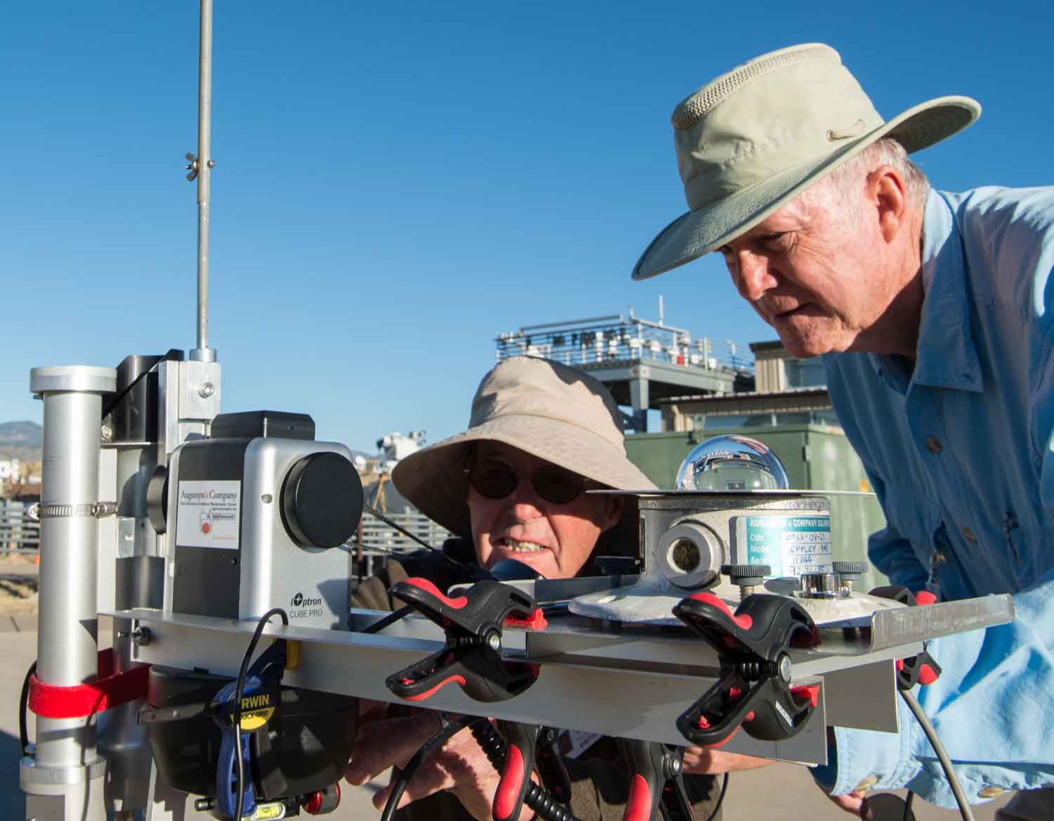 Two men hunch over solar radiation instruments outdoors.