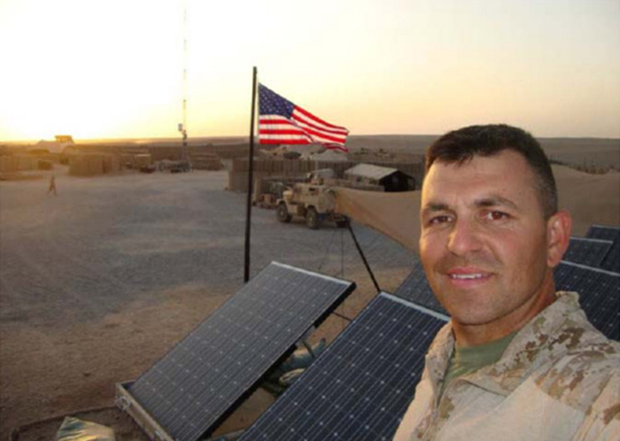A soldier stands in front of solar panels in the field.