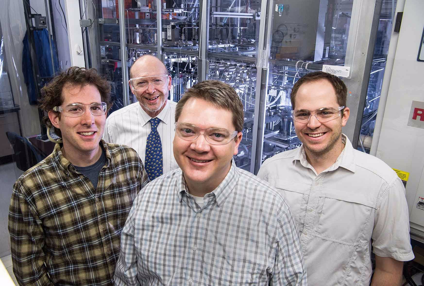 Four men stand in front of a device used to grow crystalline semiconductor structures.