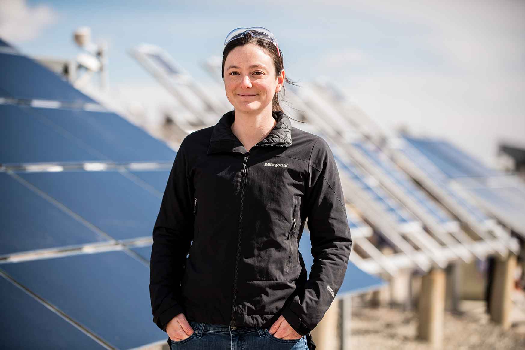 A woman stands in front of solar panels.