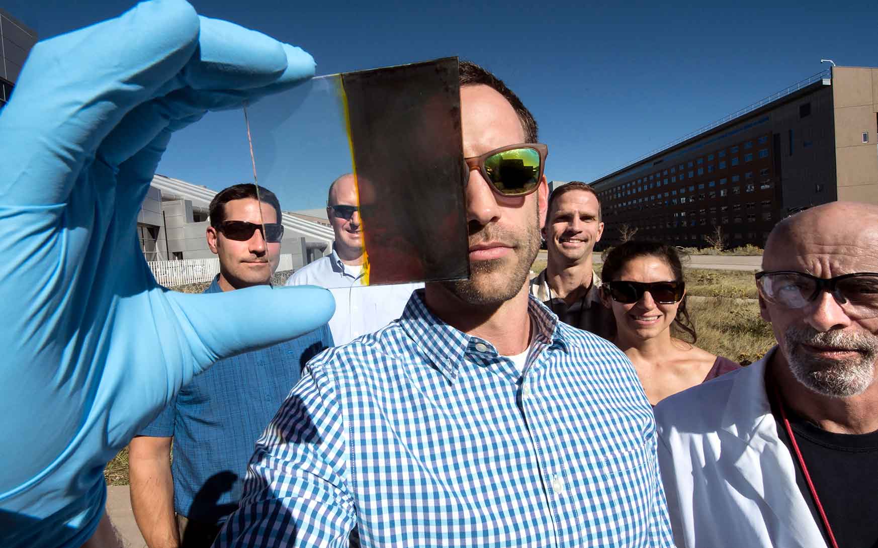 A scientist at NREL holds a piece of glass that is split between transparent and opaque.