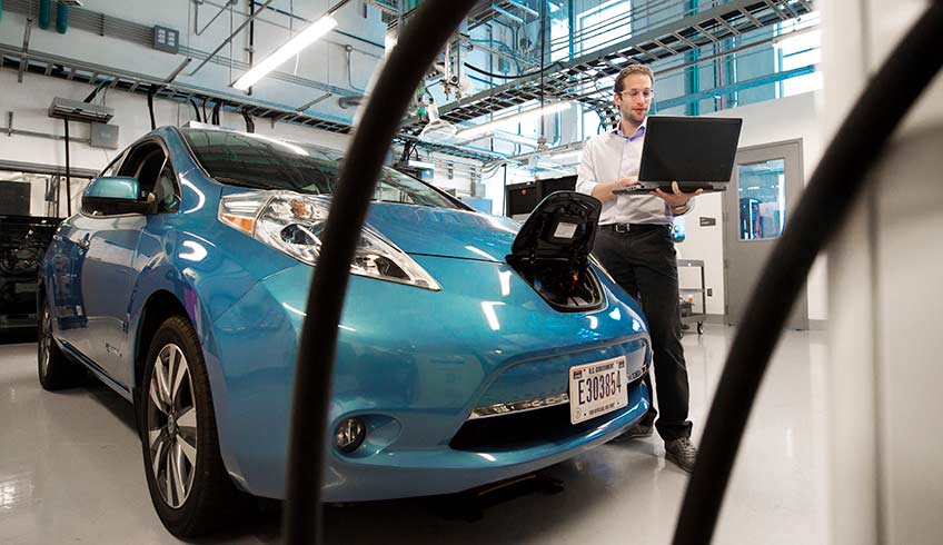 A man stands next to a car parked inside a laboratory at NREL.