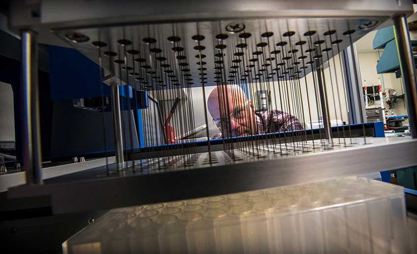 One man stands behind some laboratory equipment.