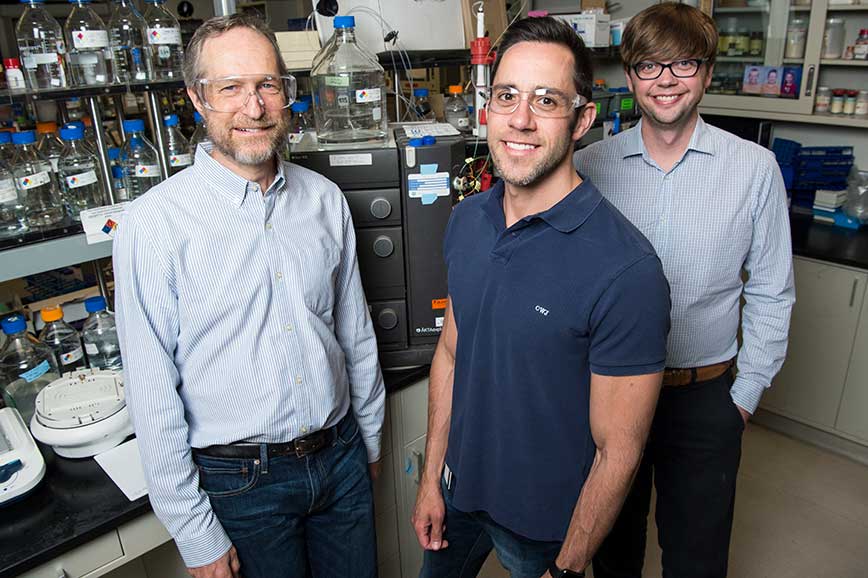 Three men stand in a laboratory.