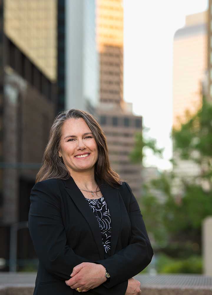 Woman in a business suit stands in front of tall buildings in downtown Denver