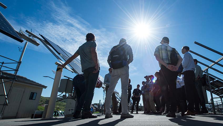 Photo of a group of people standing by solar array on a sunny day.