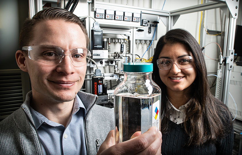 Two researchers display a container of high-performance ether diesel bioblendstock manufactured at NREL.