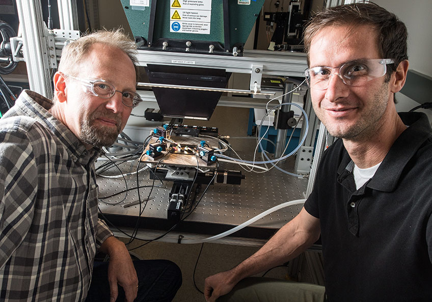 Two men stand next to a piece of testing equipment.