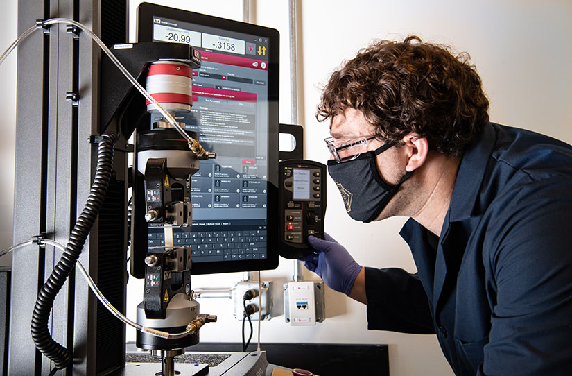 A researcher working with scientific equipment that tests tensile strength of plastic
