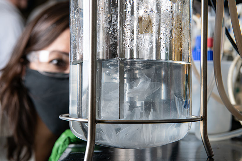 Photo of a woman examining a container of clear liquid in a lab