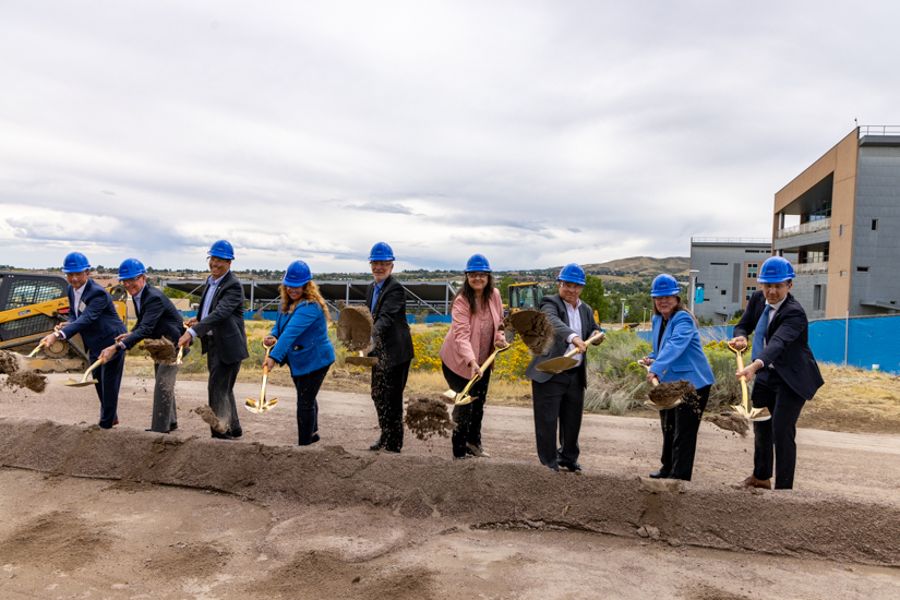 Nine people with shovels and hard hats toss dirt into a pile.