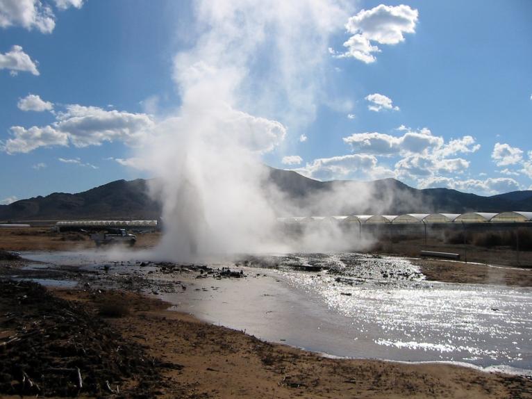 An image shows a steaming stream of water in the foreground, with a series of commercial greenhouses in the background.