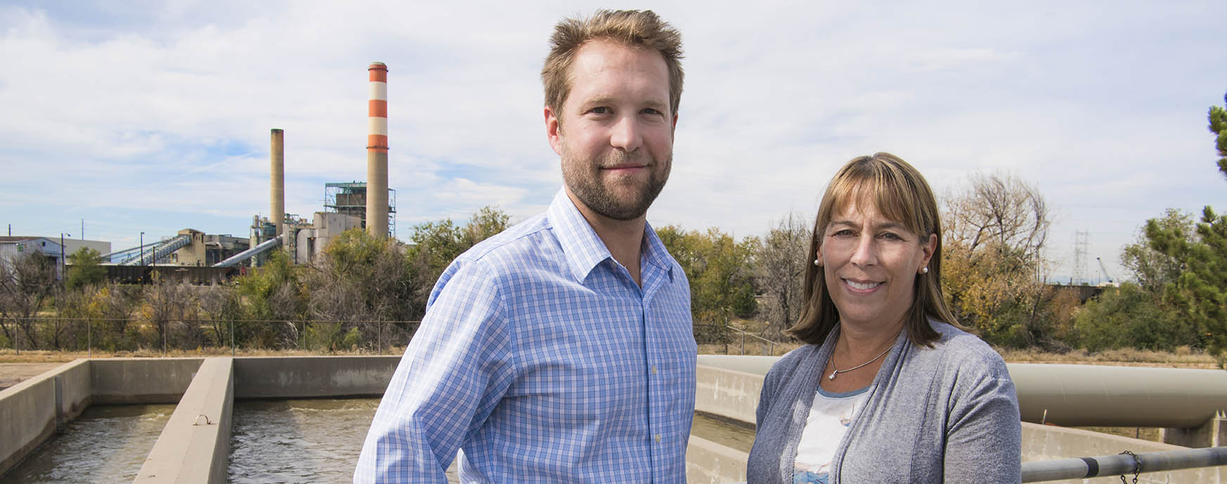 Photo of man and woman standing outside with power plant in background.