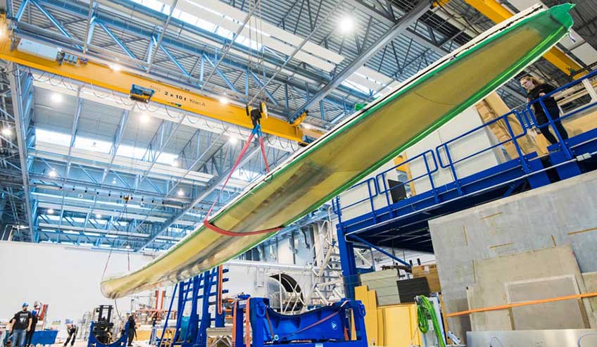 A large wind turbine blade is suspended from a high, metal ceiling.
