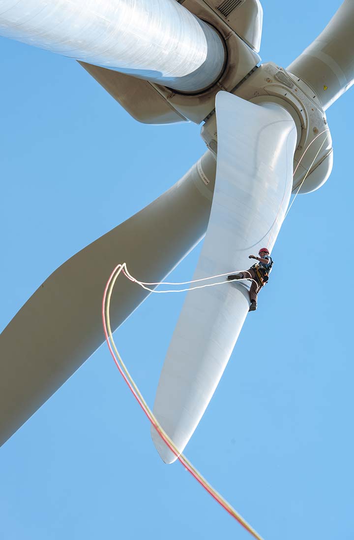 A worker repells down the blade of a large wind turbine