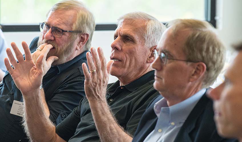 A man holds up hands to make a point while other men sit beside him in a meeting room.