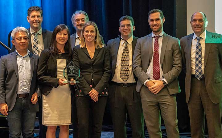 Eight people stand with award