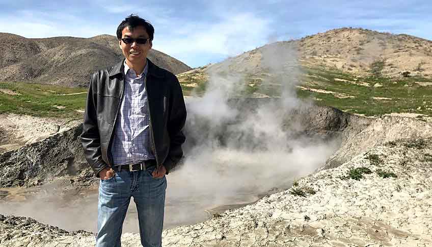 Guangdong Zhu stands in front of a hot spring, located near an active geothermal plant.