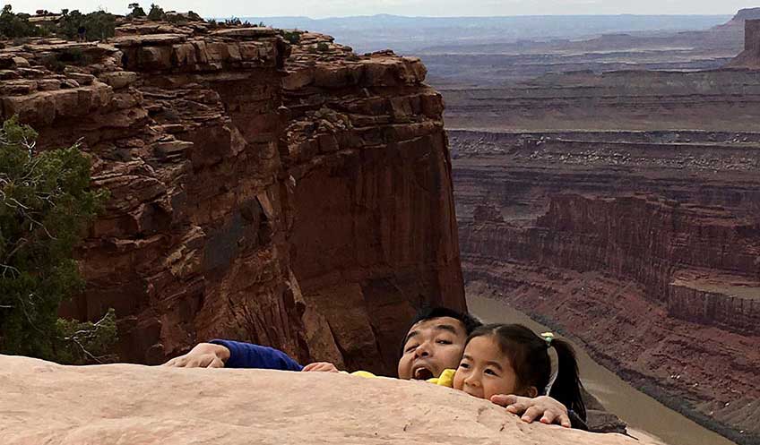 Guangdong Zhu and his daughter pose for a photo next to a desert canyon, pretending to fall in.