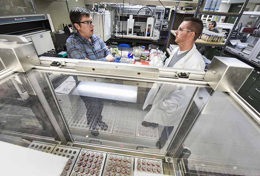 Two men speaking to each other with laboratory equipment surrounding them.