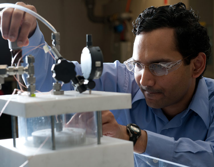 Man in blue shirt and goggles works on a scientific apparatus in a laboratory.