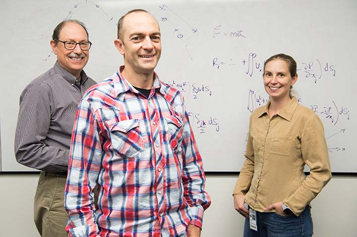 Two men and a woman stand in front of a board filled with mathematical equations.