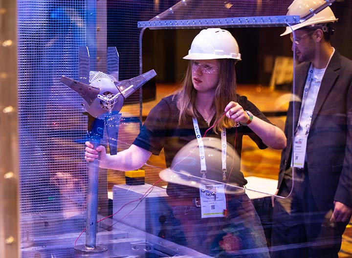 Female student wearing a hard hat and safety glasses sets up her team's model wind turbine in the wind tunnel.