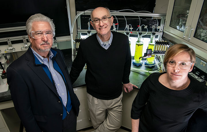 One woman and two men in a laboratory standing in front of scientific equipment.