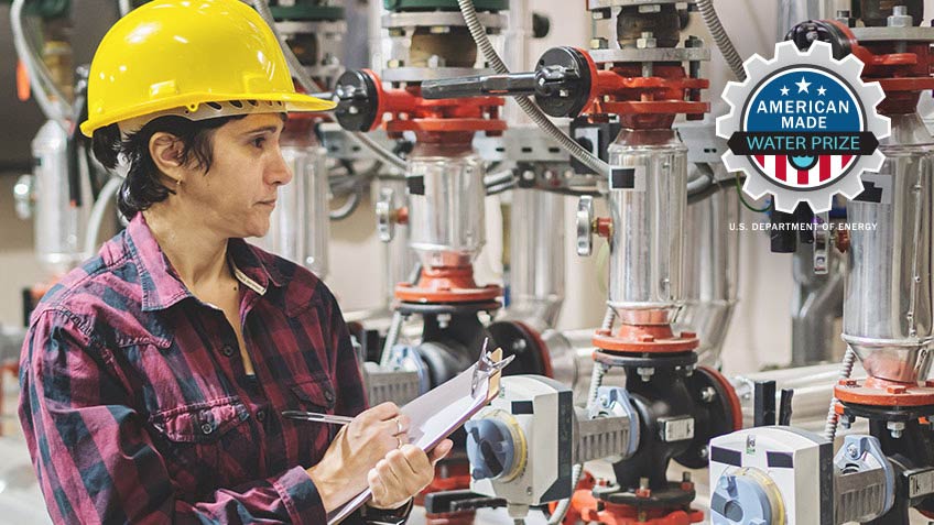 Woman holds a clipboard while standing next to a machine in a hard hat. 