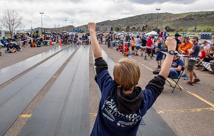 A young student celebrates his model car crossing the finish line at the middle school electric car competition.
