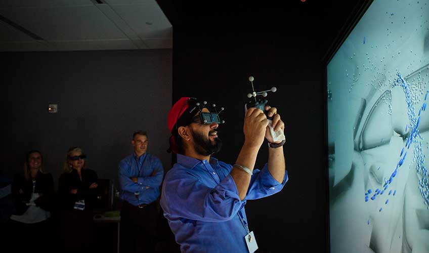 A group with virtual reality goggles in a virtual reality lab looking at three-dimensional screen displaying water droplets on a white background.