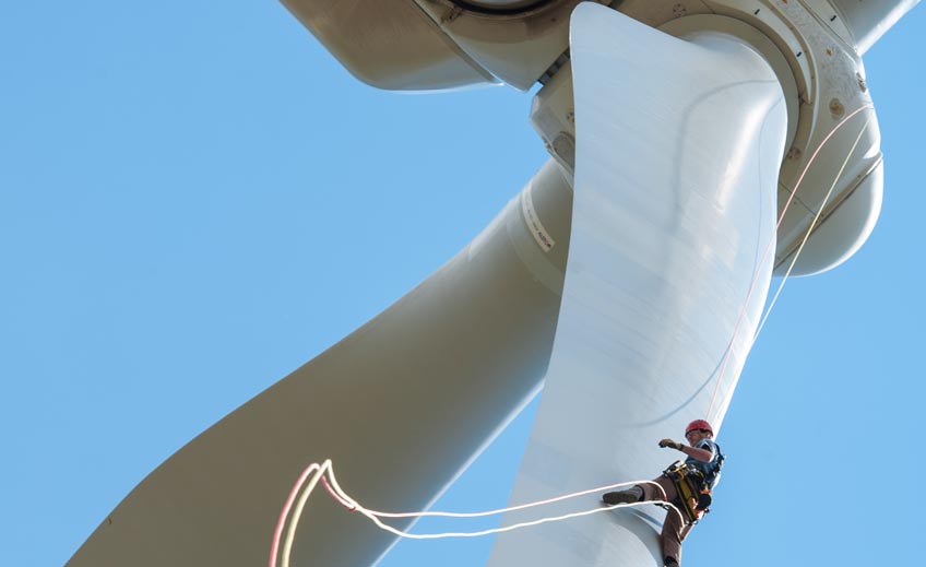 Man inspects a wind turbine by rappelling down the blades.