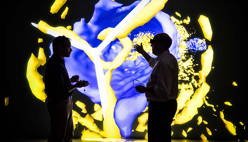 Two men in 3D goggles looks at a large wind turbine visualization in a dark room