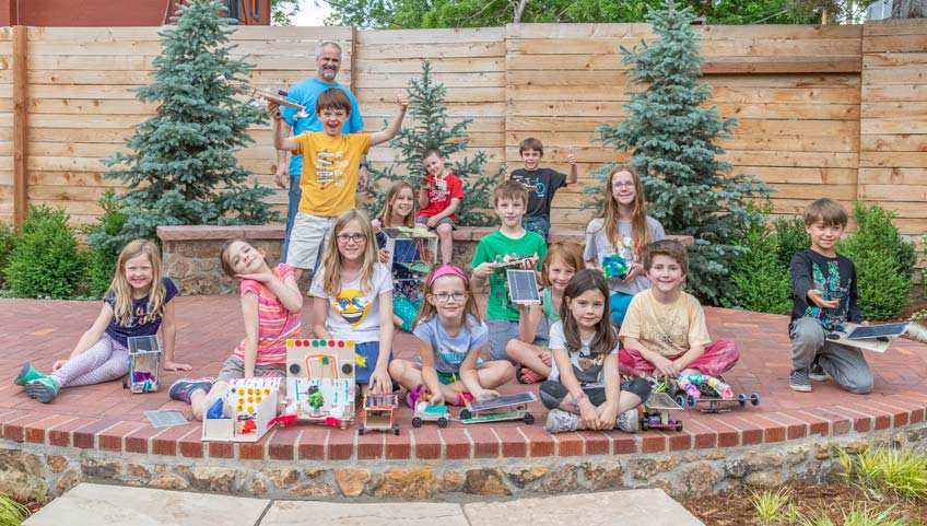 Photo of a group of children sitting on a brick patio and holding small sculptures.