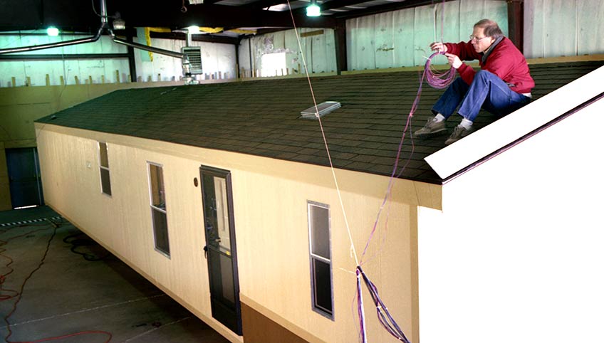 Ron Judkoff sits on the roof of a mobile home, working with a coil of wire.