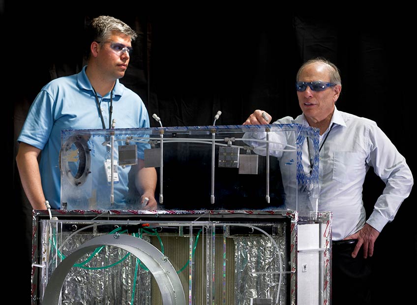 Ron Judkoff and Eric Kozubal stand wearing protective eyewear behind a piece of experimental HVAC equipment.