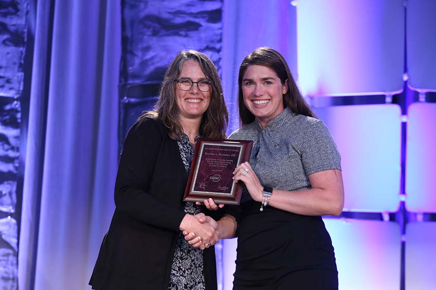 Rachel Romero receives a plaque from Sheila Hayter while shaking hands.