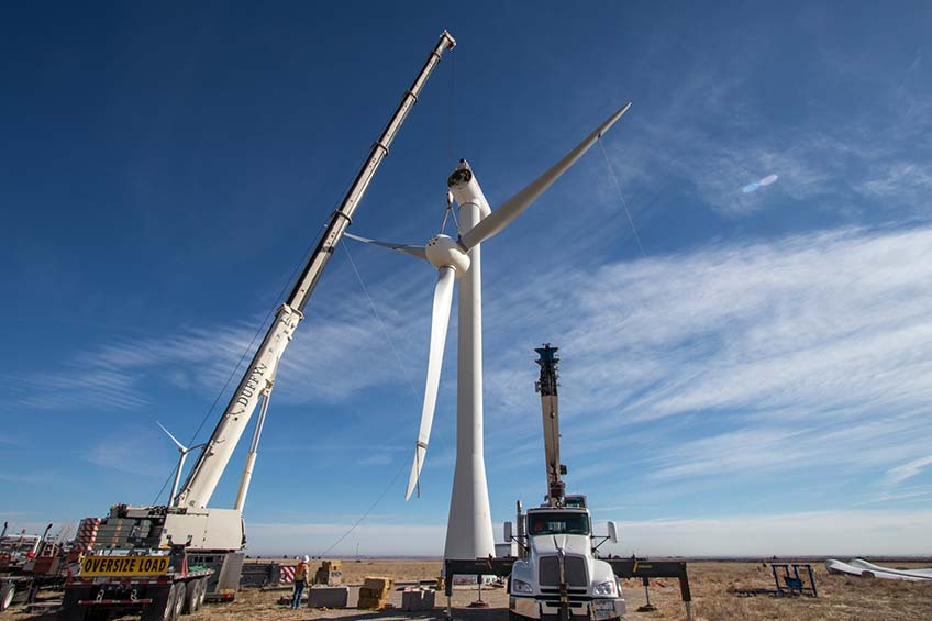 A crane lifts a turbine rotor into place on a wind turbine.