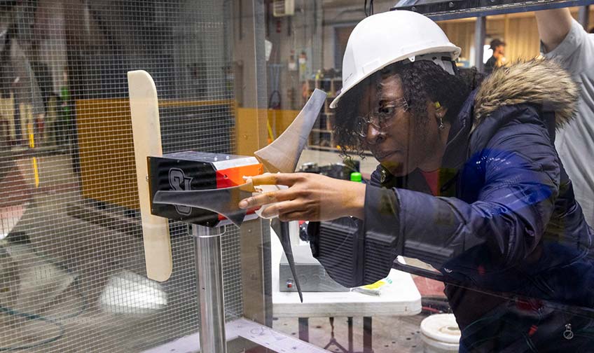 A college student in a hard hat examines a miniature competition wind turbine.