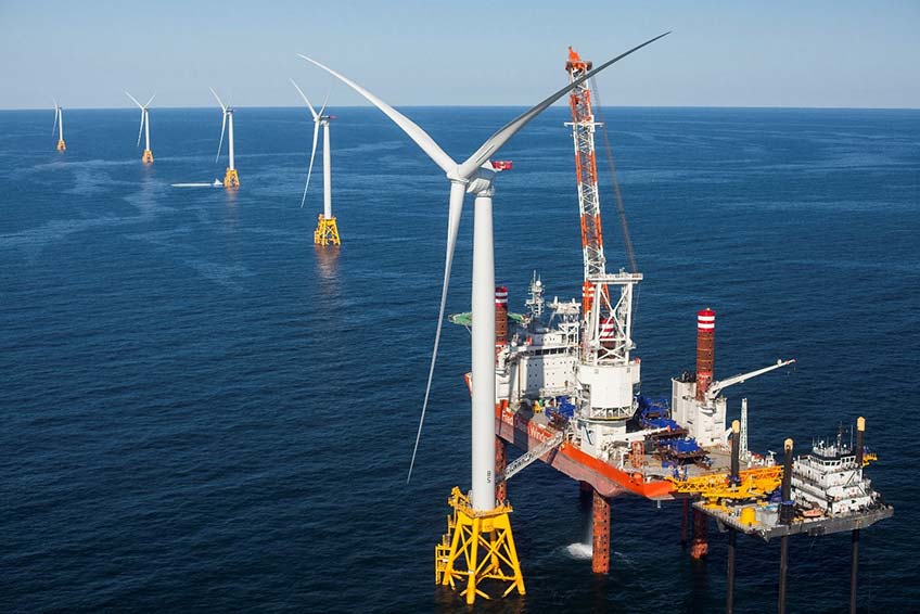 A platform rests next to a wind turbine to allow for construction out in the ocean.
