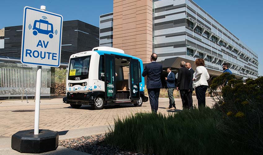 Photo of people standing next to a 12-passenger automated vehicle.