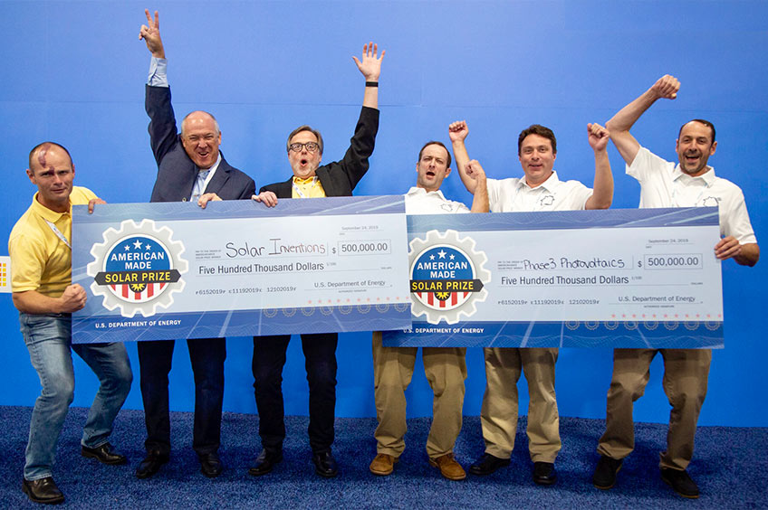 Individuals from two winning teams stand on-stage holding large checks.