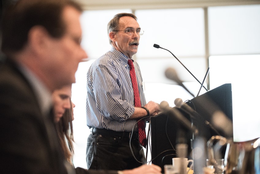 A man speaks at a podium microphone in front of people.