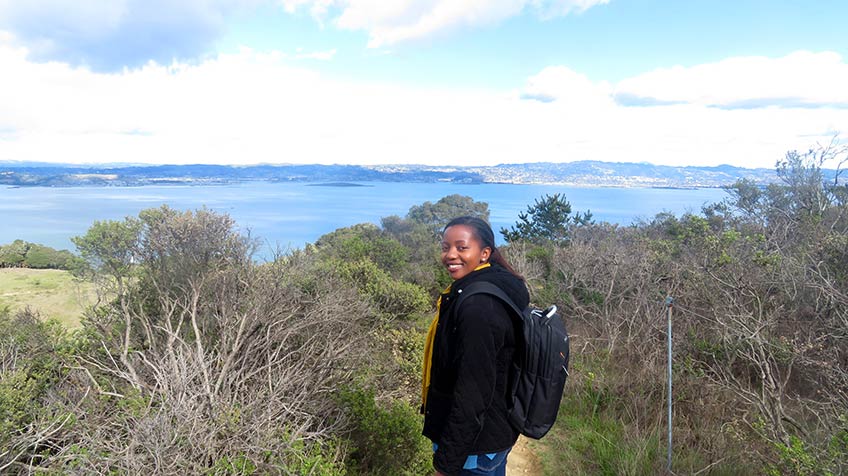 NREL researcher Juliette Ugirumurera stands in front of crass and brush with a lake in the background.