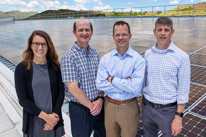A group of researchers stand in front of an array of solar panels.