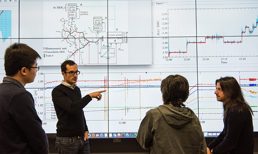 Four researchers review data on a large computer screen.