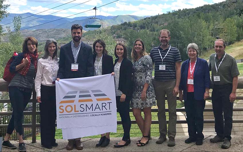 SolSmart community representatives pose with Megan Day outside with mountains and a chair lift in the background.