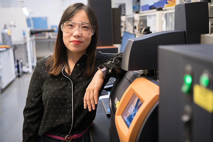 Shuang Cui poses next to a scanning calorimeter in the lab.