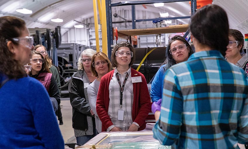 A group of women in the manufacturing industry listen as NREL research engineer Robynne Murray demonstrates an infusion process using thermoplastic resins.